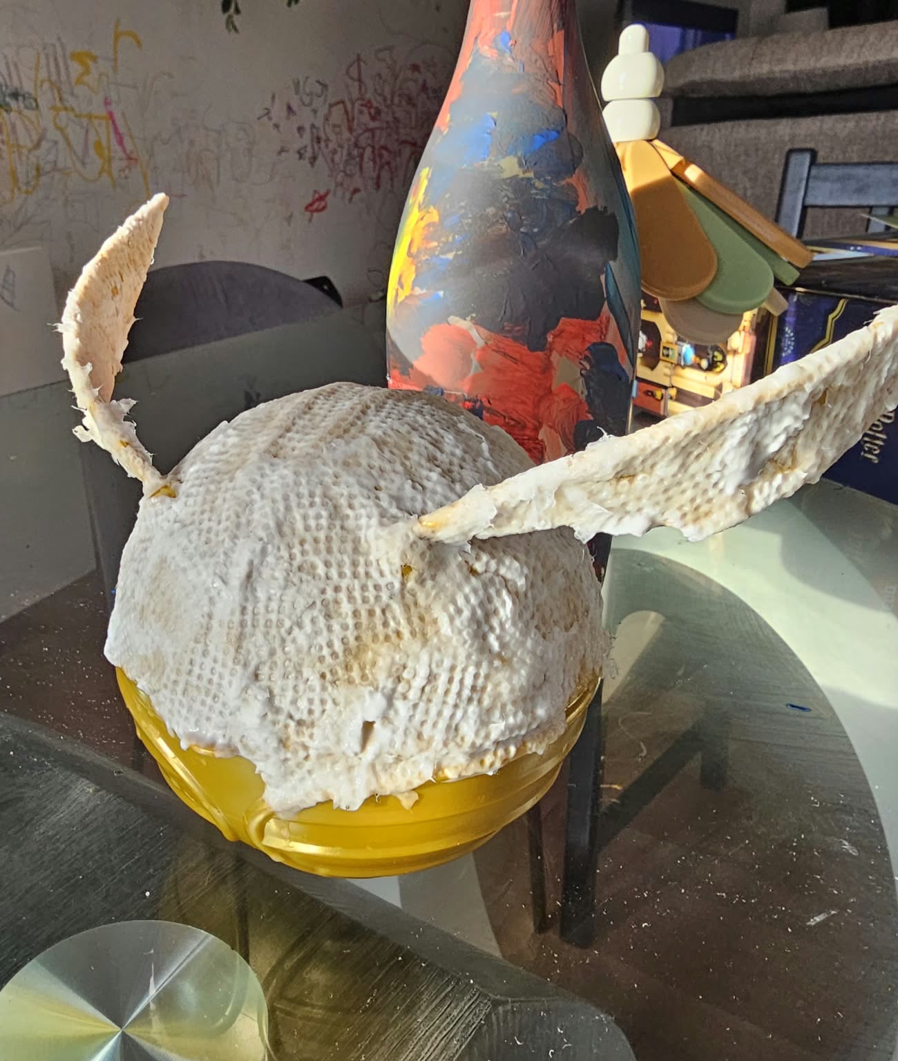Side view of the Golden Snitch holder with its body and wings covered in textured paper towel and glue.