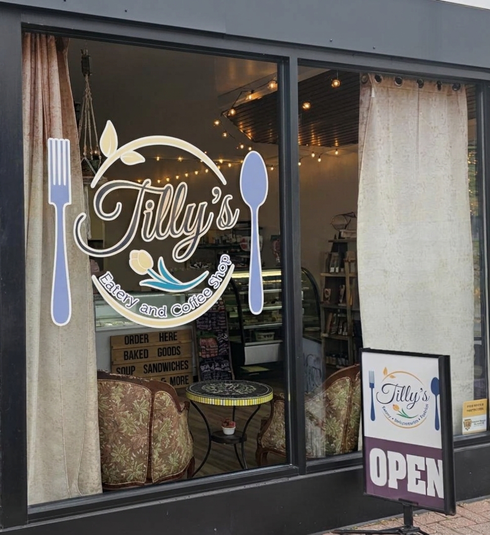 Tilly’s Eatery and Coffee Shop window logo, framed by curtains and warm lights, with an open sign outside.
