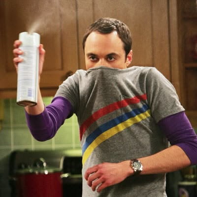 Jim Parsons as Sheldon Cooper holding an aerosol spray can with his T-shirt pulled over his nose in The Big Bang Theory.