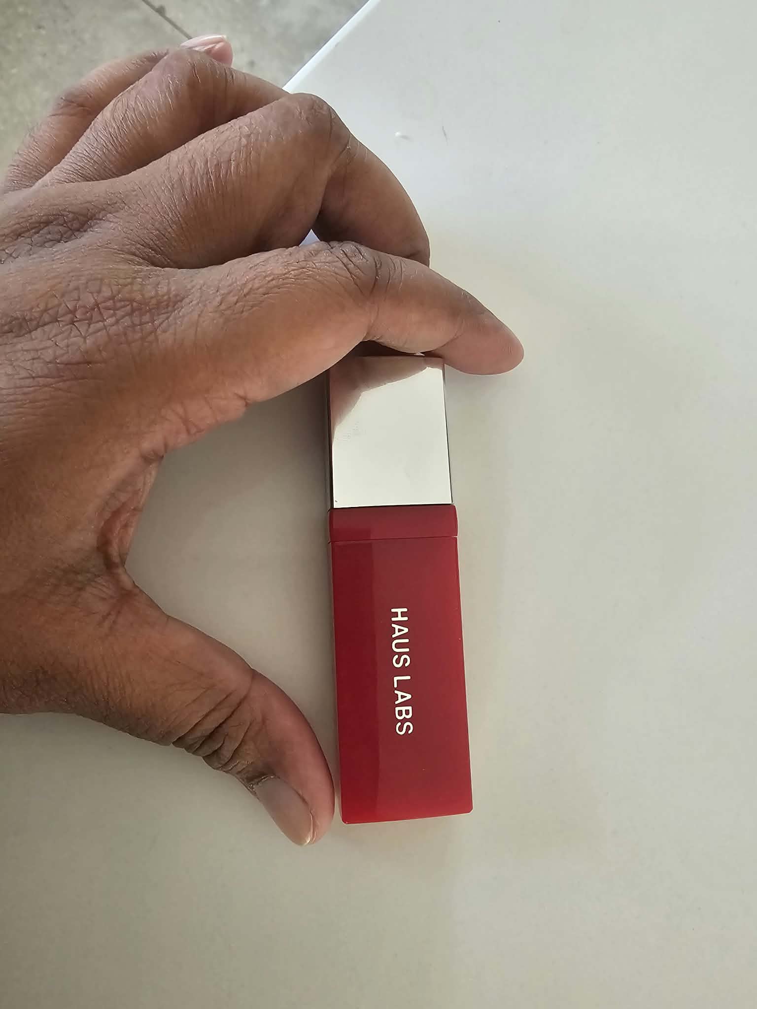 A hand holding a ruby-red tube of Haus Labs Atomic Shake High-Shine Longwear Lip Lacquer.