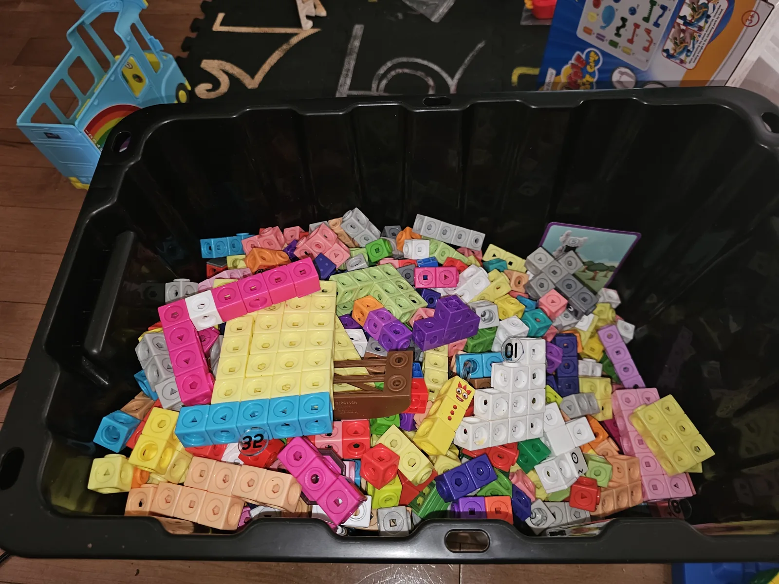 Open black storage box overflowing with colourful Numberblocks MathLink cubes and character pieces in a family living room.