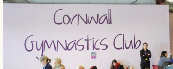 The Cornwall Gymnastics Club sign above coaches and gymnasts inside the gym.